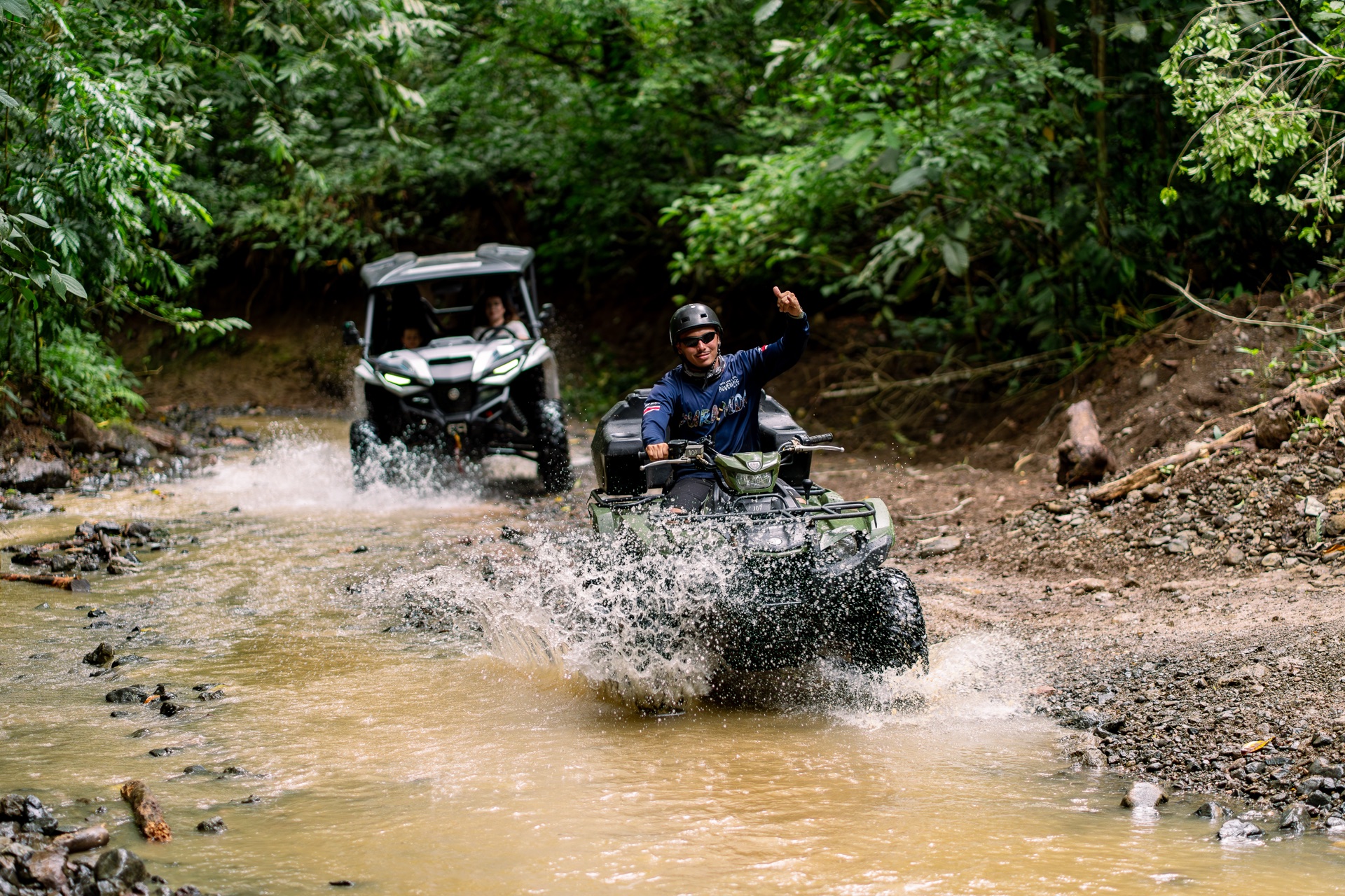 ATV powering through muddy water with a dramatic splash on a Jacó jungle trail